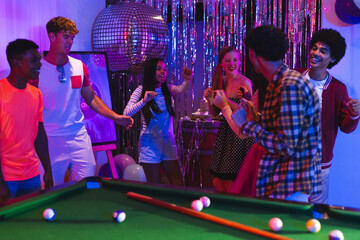 Fototapeta premium Teens celebrating around pool table with disco ball and festive decorations