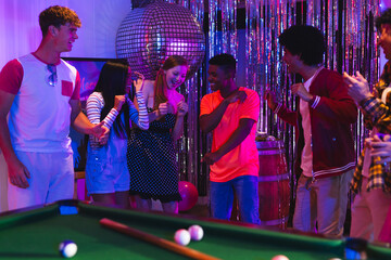 Teens dancing joyfully at party near pool table under disco ball lights © WavebreakMediaMicro
