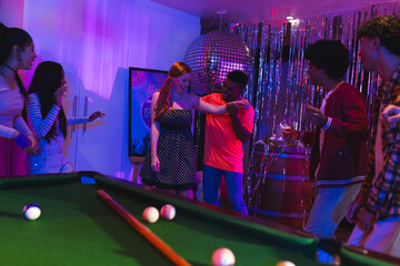 Teens celebrating at party, dancing near pool table under disco ball lights © WavebreakMediaMicro