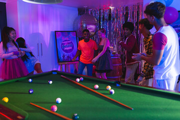 Teenagers enjoying vibrant party playing pool and dancing under disco lights © wavebreak3