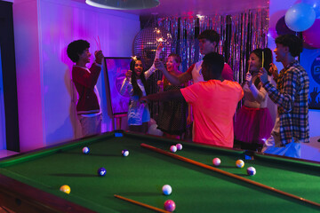 Fototapeta premium Teenagers celebrating around pool table with colorful lights and festive decorations