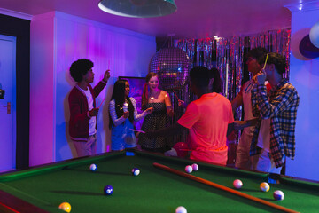 Fototapeta premium Teenagers celebrating around pool table with colorful lights and festive decorations