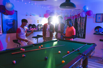 Fototapeta premium Celebrating birthday, teenagers playing pool in festive room with balloons and decorations