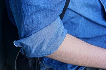 one hand of a man with a blue rolled up sleeve of a cotton shirt on a summer street