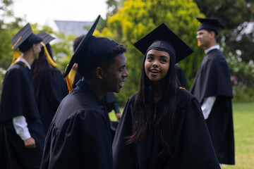 Graduating students in caps and gowns celebrating together outdoors, smiling happily