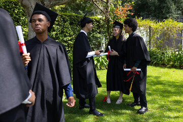 Graduating students in caps and gowns celebrating together outdoors with diplomas