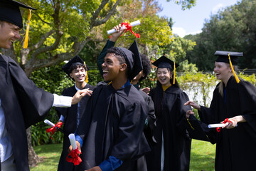 Graduating students holding diplomas, wearing caps and gowns, celebrating outdoors