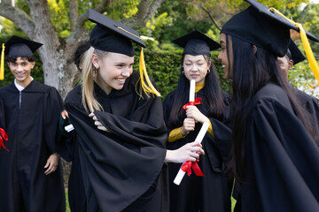 Graduating students in caps and gowns celebrating with diplomas outdoors