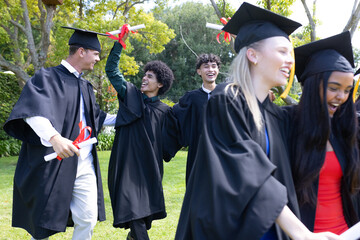 Graduating students in caps and gowns celebrating outdoors, holding diplomas proudly