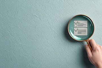 Hand holding a magnifying glass over an illustration of a checklist on a textured surface.