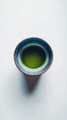 A top-down view of a matcha green tea cup placed on a white surface, showcasing the vibrant green tea in a minimalist and clean setting. The simple composition highlights the calm and refreshing natur