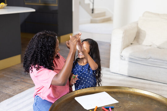 African American mother and daughter high-fiving while drawing together at home