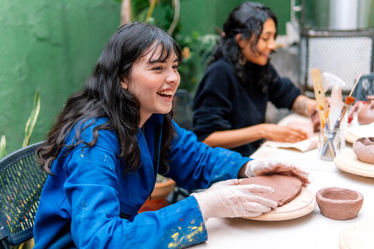 Female potter skillfully shaping clay on a wooden plate, fully immersed in the creative process during a pottery workshop