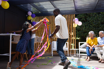 Celebrating outdoors, family dancing with colorful streamers, sharing joyful moments together © WavebreakMediaMicro