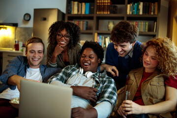 Young and diverse group of friends watching a movie on laptop in the living room on the couch