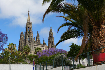 Neo-Gothic Church of San Juan Bautista in Arucas, Gran Canaria, with palm trees, blossoms and blue...