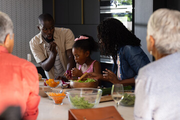 Family cooking together in kitchen, sharing laughter and preparing fresh salad © WavebreakMediaMicro