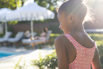 Young girl in pink dress enjoying sunny day by poolside with family