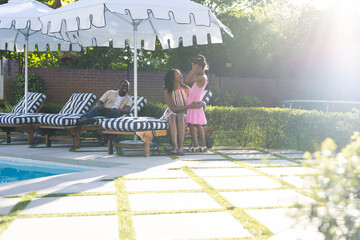 Family enjoying sunny day by pool, mother and daughter sharing joyful moment