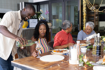 Outdoor family meal, man pouring wine while everyone smiling and talking together