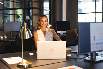 Smiling woman working late at office desk with laptop and coffee