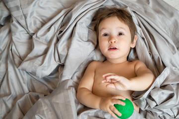 Top view of cute caucasian toddler playing ball in bed. 