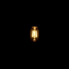 Glowing Filament Light Bulb in Darkness: Symbol of Hope and Creativity