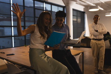 Colleagues celebrating success with laptop and documents in modern office at night