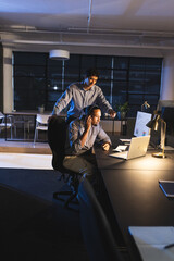 Businessmen working late in office, discussing project on laptop with focus