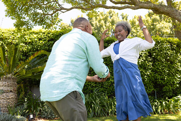 Senior couple dancing joyfully in garden, enjoying sunny day together © wavebreak3
