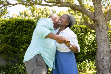 African American senior couple dancing joyfully under tree in sunny garden © wavebreak3