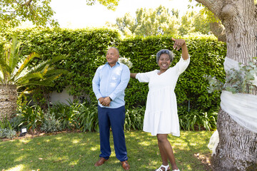 Fototapeta premium Senior couple enjoying sunny day in garden, woman dancing joyfully beside partner