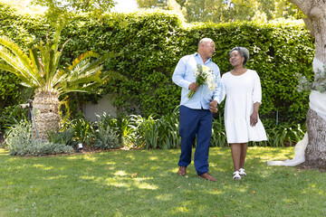 Senior couple walking in garden, holding hands and smiling at each other