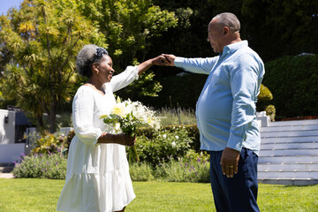 Senior couple dancing joyfully in garden, holding hands and smiling brightly © wavebreak3