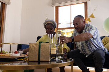 Senior couple celebrating at home with cake and champagne, enjoying special occasion