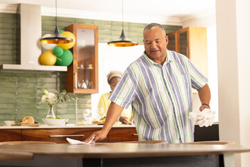 African American man cleaning kitchen counter while smiling, woman in background