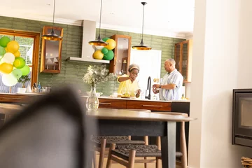Selbstklebende Fototapeten In kitchen, African American senior couple preparing meal, smiling warmly together © wavebreak3
