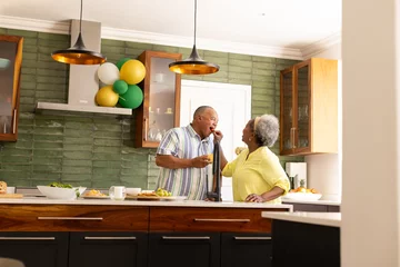 Selbstklebende Fototapeten Senior couple in kitchen enjoying conversation and preparing meal together © wavebreak3