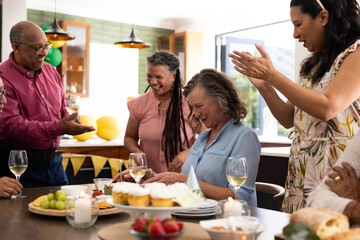 Senior friends celebrating birthday at home, clapping and smiling around table