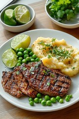 Grilled steak served with green peas, mashed potatoes garnished with herbs, and lime wedges on a white plate, fresh cilantro in background