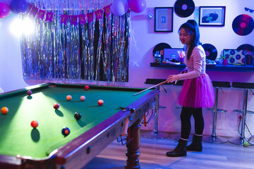 Fototapeta premium Young woman playing on pool table in home party room, with birthday decorations, copy space