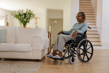 Senior African American woman sitting in wheelchair in living room, with flower vase, copy space
