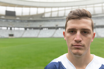 Male soccer player standing on stadium pitch, wearing blue-and-white jersey under overcast sky