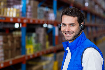 Smiling warehouse man coordinating inventory checks in aisles of boxes with headset, copy space
