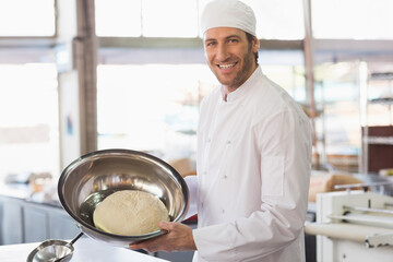 Holding dough in stainless steel bowl, male chef working at counter in bakery kitchen, copy space