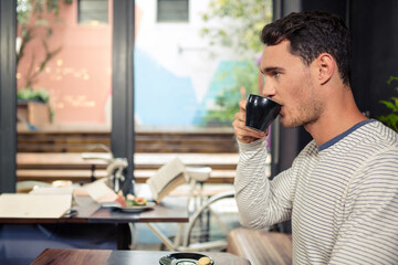 Man sipping coffee at table in modern cafe, with black coffee cup and macarons, copy space
