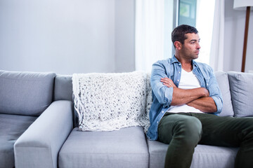 Obraz premium Sitting man looking outside on grey sofa in living room, with knitted blanket, copy space