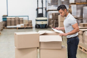 Inspecting man holding clipboard and pen in warehouse, with forklift and boxes, copy space