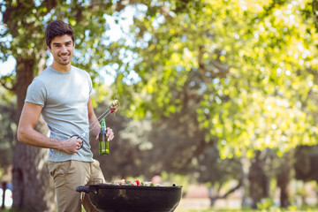 Charcoal barbecue grill cooking meat and vegetable skewers in sunlit park, with green bottle