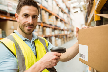 Standing male warehouse worker wearing safety vest scanning box in aisle, with handheld scanner